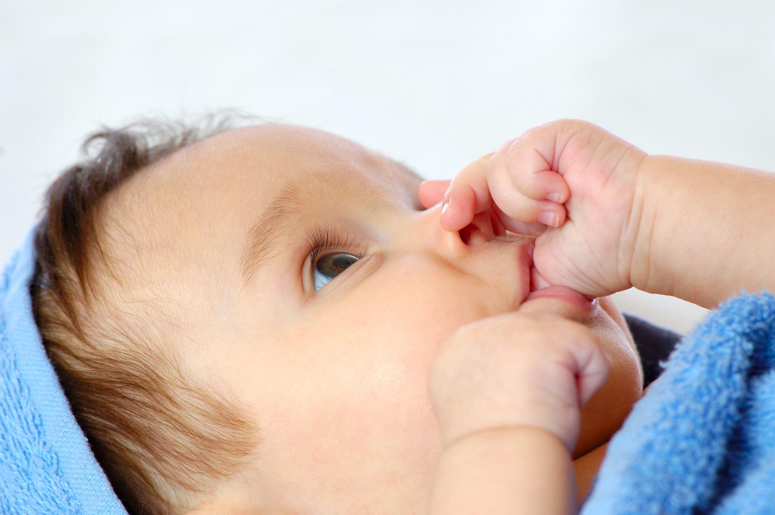 Close up of a four month old baby who has a thumb sucking habit that will eventually need addressed and stopped